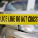 Yellow police tape reading POLICE LINE DO NOT CROSS in front of a vehicle