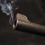 Fatal Shot: Child’s Desperate Act Close-up of a gun barrel emitting smoke against a black background