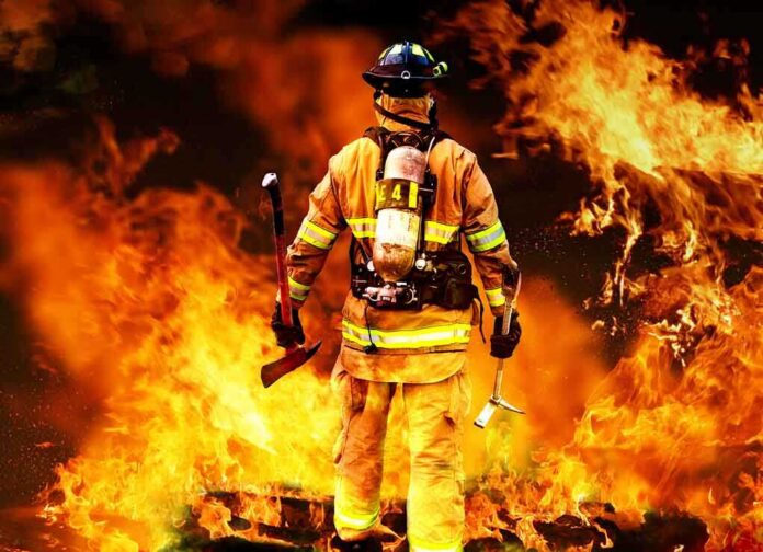 shutterstock_80081197.jpg Firefighter standing in front of a large fire, equipped with tools