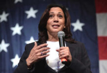Woman speaking with microphone, American flag background.