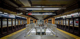 Subway station platform with directional signs overhead.