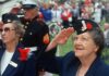 Elderly women in military attire saluting during a veterans ceremony