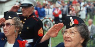 Elderly women in military attire saluting during a veterans ceremony
