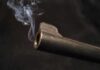 Close-up of a gun barrel emitting smoke against a black background