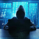 Person in hoodie using a laptop with digital code.