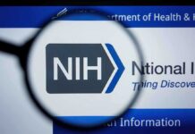 Mysterious NIH Exit — Major Role Vacant! NIH logo displayed on a digital screen, viewed through a magnifying glass