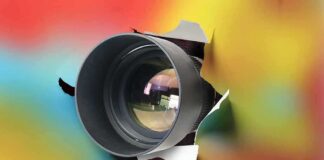 Camera lens emerging through torn colorful paper
