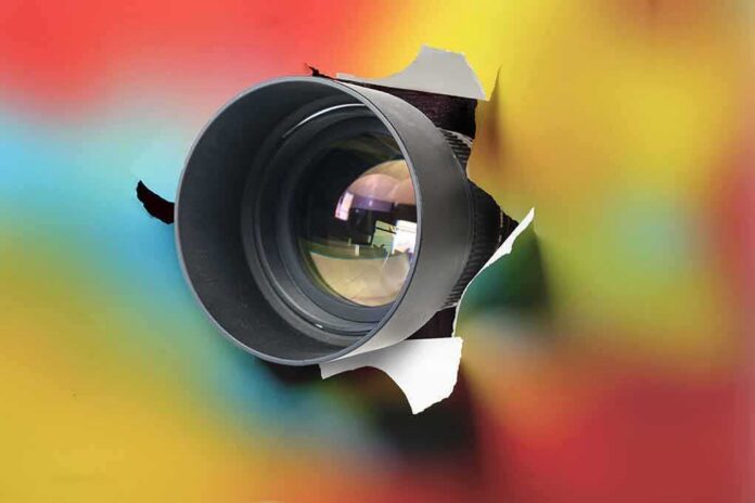 Camera lens emerging through torn colorful paper