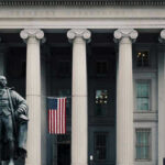 Fed Signals Longer Pain as Rate Cut Hopes Fade US Treasury Department building with statue and flag.