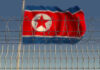 North Korea Signals Military Expansion in Factory Visit Barbed wire fence with North Korean flag behind.