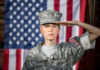 Soldier saluting in front of American flag backdrop.