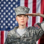 Soldier saluting in front of American flag backdrop.