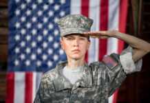 Soldier saluting in front of American flag backdrop.