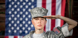 Soldier saluting in front of American flag backdrop.
