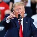 Man in suit pointing, speaking at a rally.