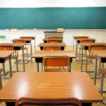Math Meltdown Alarms Top Professors Empty classroom with desks and a chalkboard.