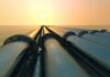 Industrial pipes extending towards the horizon over water during sunset