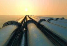 Industrial pipes extending towards the horizon over water during sunset