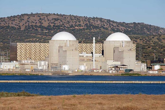 Nuclear,Power,Station,With,Two,Atomic,Reactors Nuclear power plant with domed structures beside a water body and mountains in the background