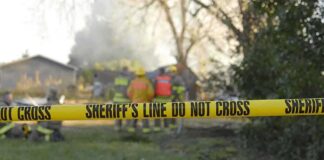 Yellow police tape marking a restricted area at a fire scene with firefighters in the background