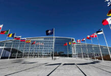 Trump Says ‘Finish the Job.’ Experts Say the Story Isn’t Over. Flags outside NATO headquarters building under clear blue sky.