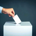Hand placing ballot into voting box.