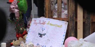 A memorial site with candles, flowers, and a hand-drawn poster