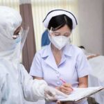nurse in PPE writing on a clipboard with colleague