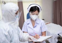 nurse in PPE writing on a clipboard with colleague