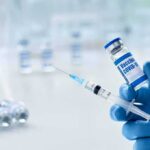 Gloved hands holding a syringe and a vaccine vial