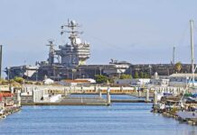 Bridge Bombings Mark Major Escalation in U.S.–Iran Conflict A large naval aircraft carrier docked in a harbor with smaller boats in the foreground