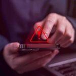 Person tapping smartphone with red warning icon