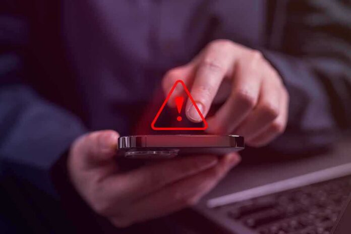 shutterstock_2307700893 Person tapping smartphone with red warning icon