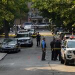 Police officers secure a residential street with patrol cars and yellow tape