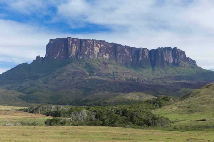 shutterstock_1017921439 Flat-topped mountain rising above green plains under a partly cloudy sky