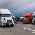 Semi trucks parked at a rest area under cloudy sky