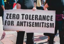 DOJ Probes ‘Unequal’ Protection Of Jews Protester holding a large sign at a rally