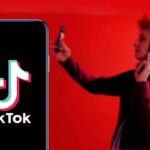Perez Hilton TikTok Live Triggers Police Rush Smartphone displaying TikTok logo with person taking selfie in red light