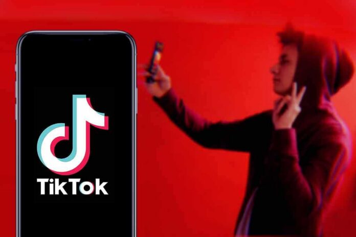 Smartphone displaying TikTok logo with person taking selfie in red light