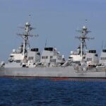 Three gray naval destroyers docked side by side at a pier