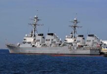 Trump’s Iran Threat Raises Civilian Target Fears Three gray naval destroyers docked side by side at a pier