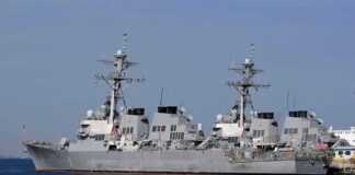 Three gray naval destroyers docked side by side at a pier