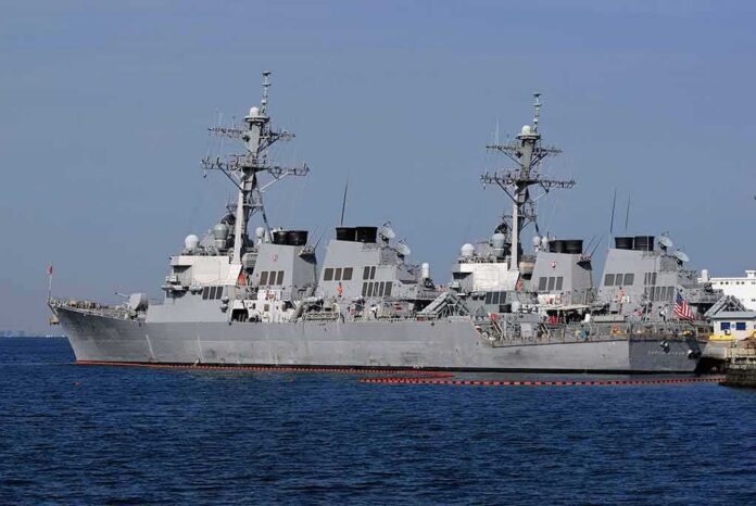 shutterstock_1626607414 Three gray naval destroyers docked side by side at a pier