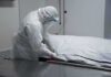 Healthcare worker in PPE zipping a body bag on a gurney