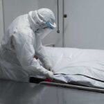 Healthcare worker in PPE zipping a body bag on a gurney