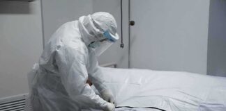 Healthcare worker in PPE zipping a body bag on a gurney