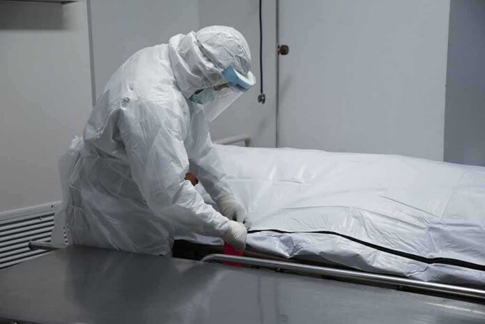 Healthcare worker in PPE zipping a body bag on a gurney