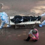 health workers in PPE move a body on a stretcher