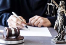 Congressman’s Son Faces 5 Felony Charges Judge writing at desk with gavel and Lady Justice statue