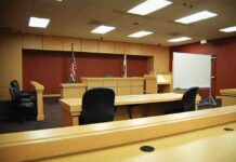 Venue Twist Freezes High-Stakes Prosecution Interior view of an empty courtroom with wooden furniture and American flags
